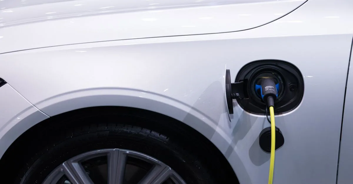 A white electric car is plugged in for charging, close-up view of the charging port.