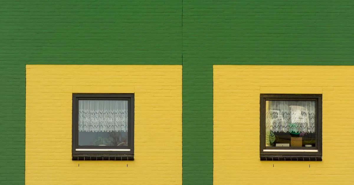 Vibrant green and yellow brick wall featuring two symmetrical windows.