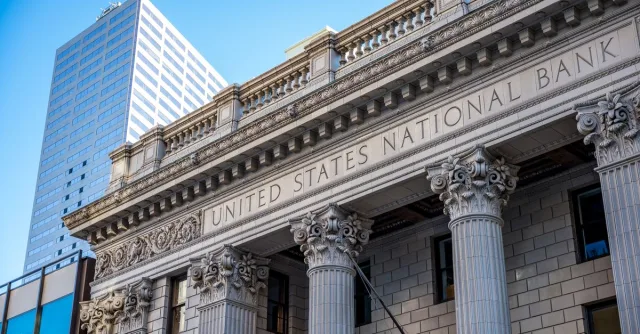 Exterior of historic national bank with decorative elements on classic columns located in city with modern building against blue sky