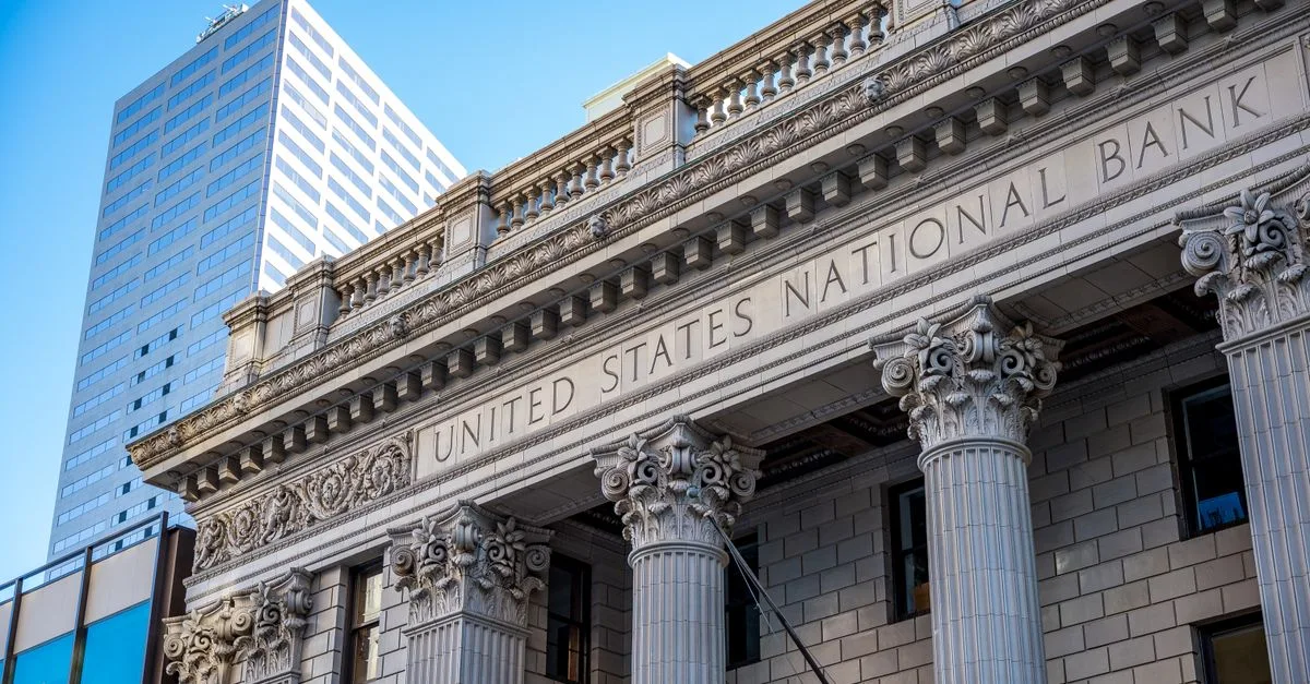 Exterior of historic national bank with decorative elements on classic columns located in city with modern building against blue sky