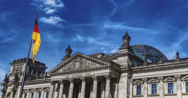 Historic Reichstag in Berlin under a vibrant blue sky, featuring the German flag.
