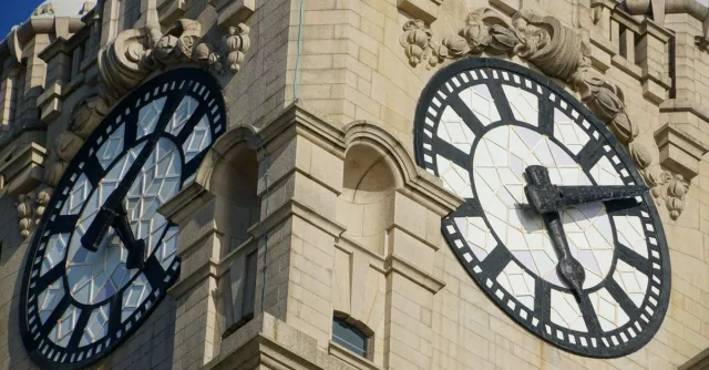 Detailed view of ornate clock faces on a historic stone tower captured in bright sunlight.