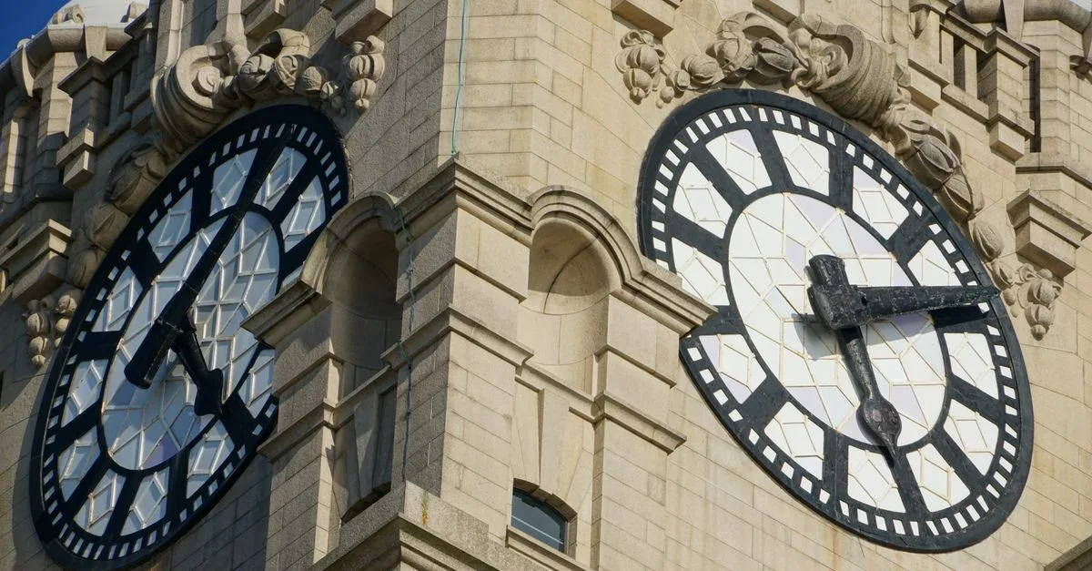 Detailed view of ornate clock faces on a historic stone tower captured in bright sunlight.