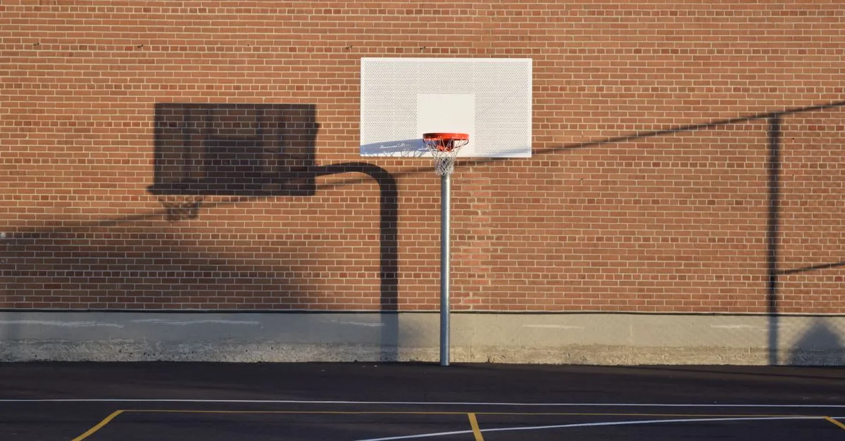 Empty outdoor basketball court with hoop and shadow against brick wall