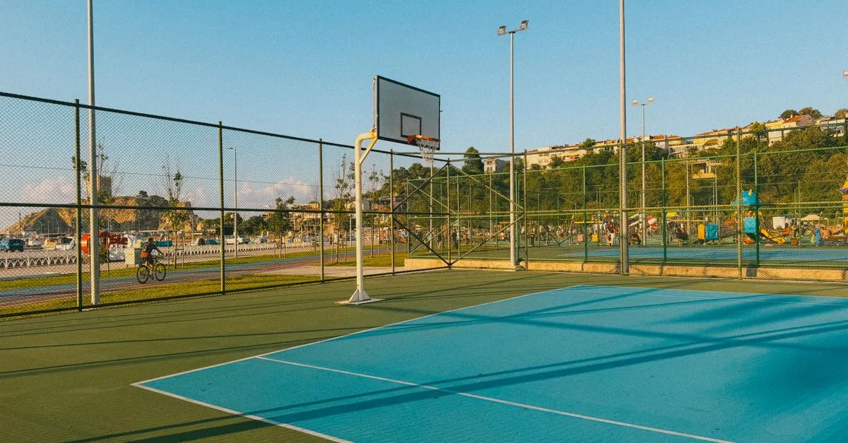 An empty outdoor basketball court with a scenic background under a clear blue sky during the daytime.
