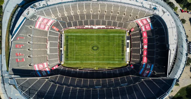 Top view of an empty soccer stadium with green field, showcasing seating arrangement under clear daylight.