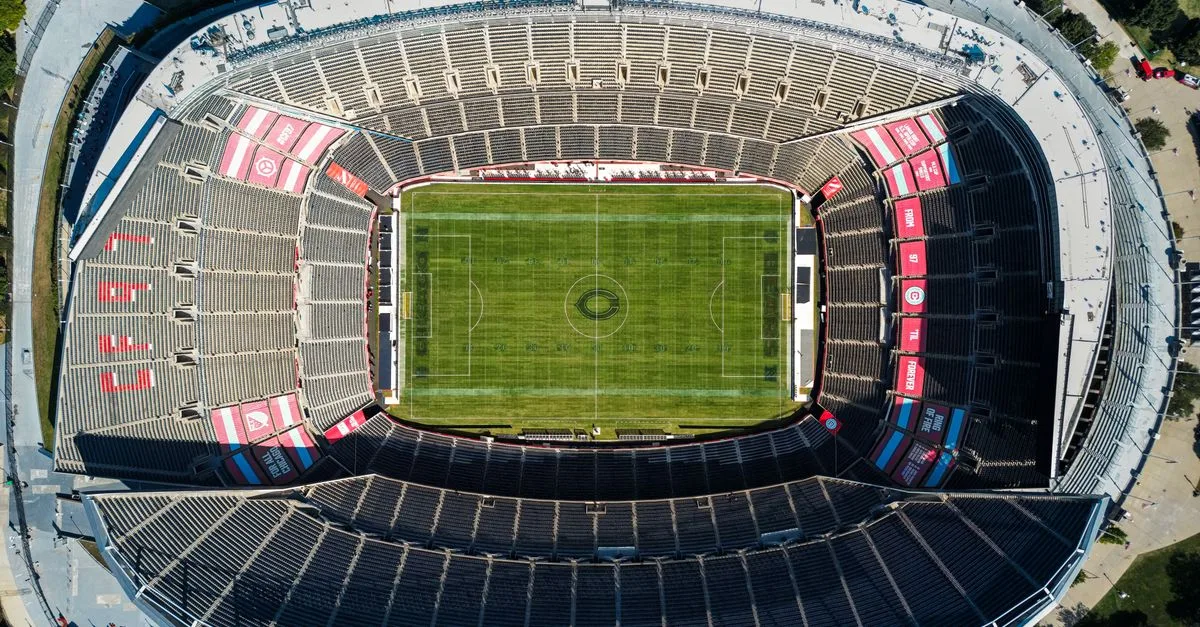 Top view of an empty soccer stadium with green field, showcasing seating arrangement under clear daylight.