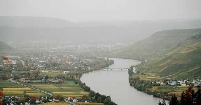 High angle of river flowing in highlands with small settlements on shores covered with dense haze