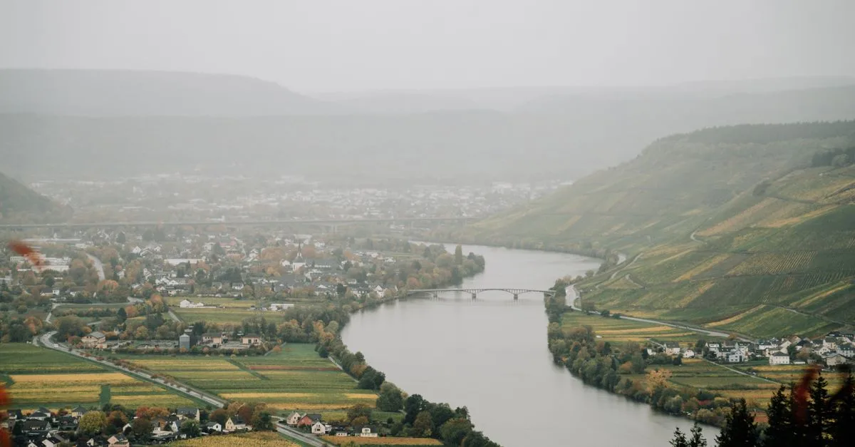 High angle of river flowing in highlands with small settlements on shores covered with dense haze