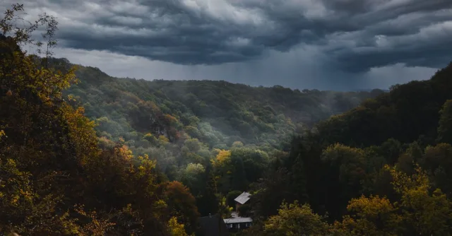 Dramatic storm clouds over a lush forest valley, highlighting vibrant autumn foliage.