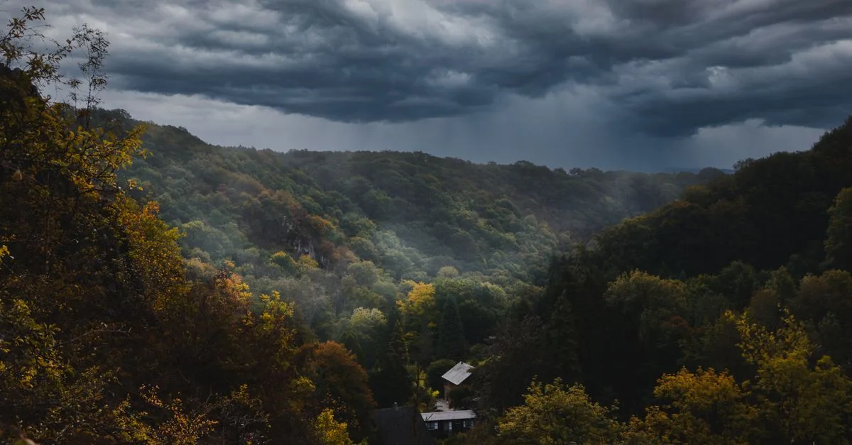 Dramatic storm clouds over a lush forest valley, highlighting vibrant autumn foliage.