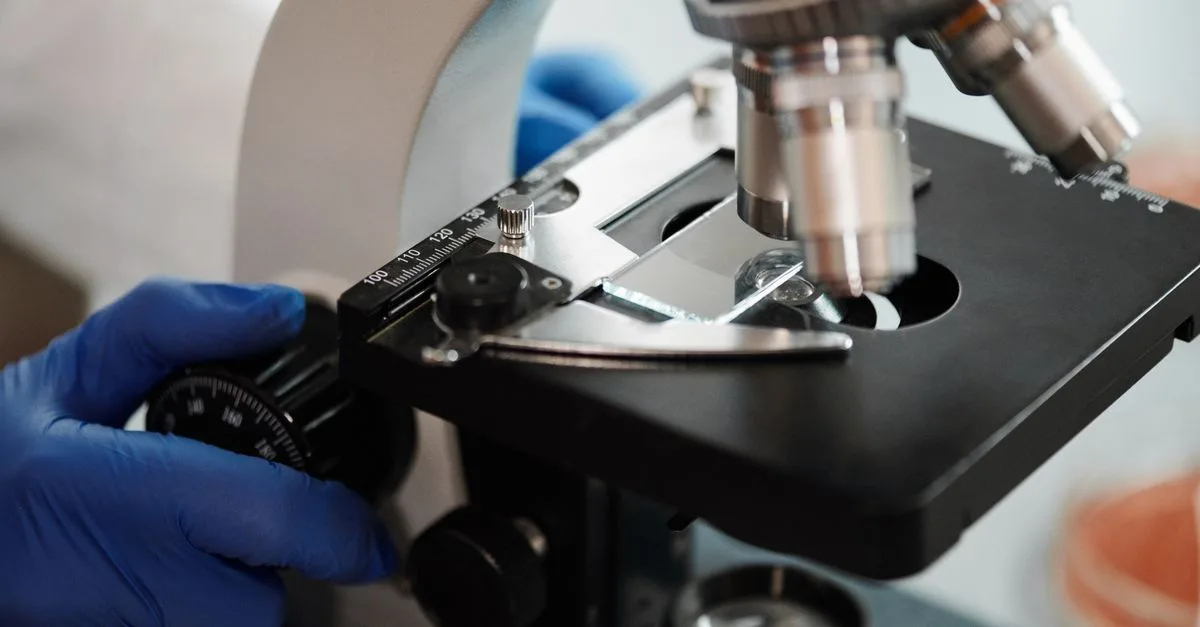 Close-up image of a scientist's gloved hand adjusting a microscope in a research lab.