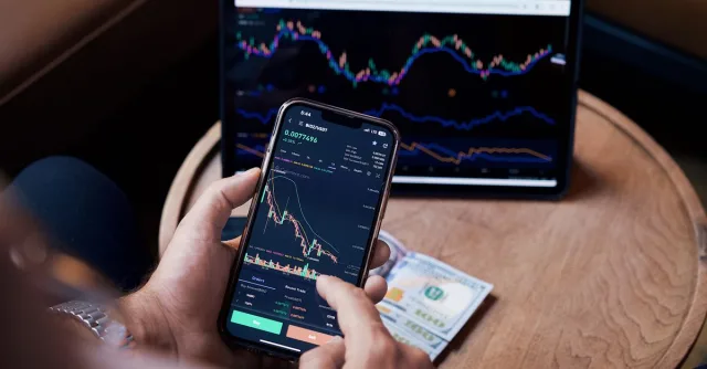 Close-up of a person trading stocks using a smartphone and a tablet.