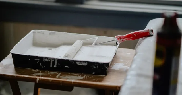 A paint roller and tray with white paint on a wooden table, indicating a renovation work.