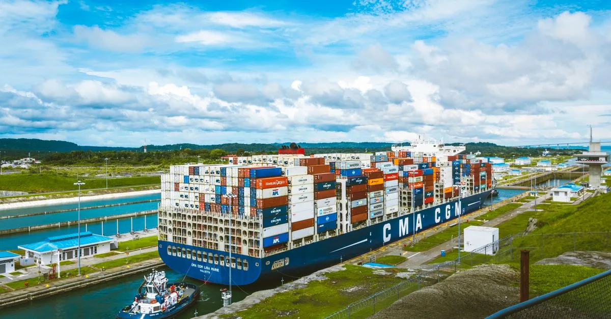 A vast cargo ship passes through the Panama Canal on a bright day, showcasing global trade.