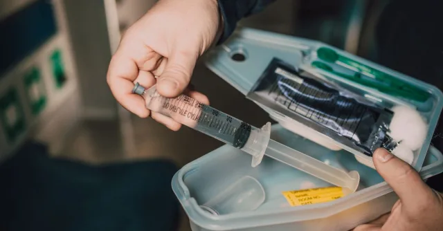 Close-up of a hand holding a syringe from a medical kit with various supplies.