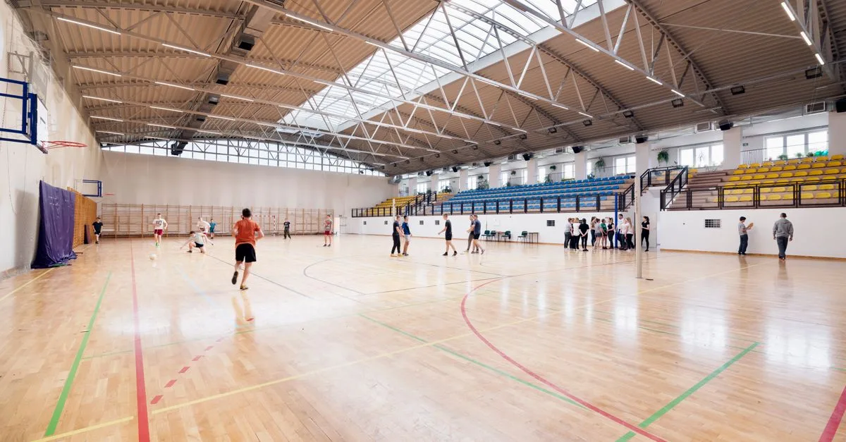 Wide-angle view of an indoor basketball court with players practicing and engaging in sports activities.