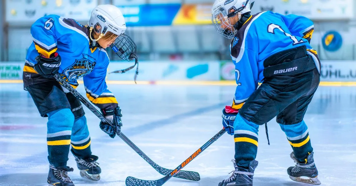 Two young athletes face-off during an ice hockey game in an indoor rink.