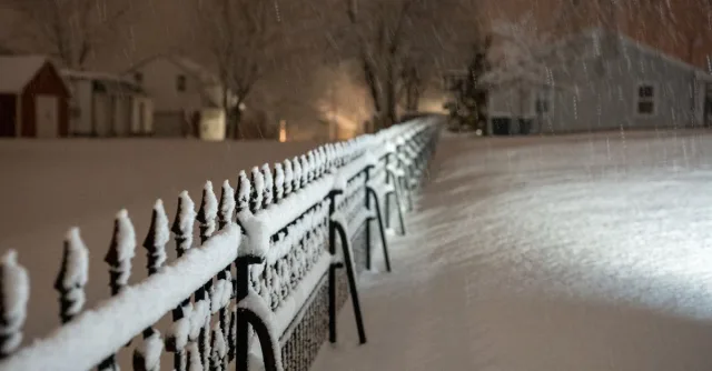 A peaceful winter night with snowfall covering fences and homes in Wabasha, MN.