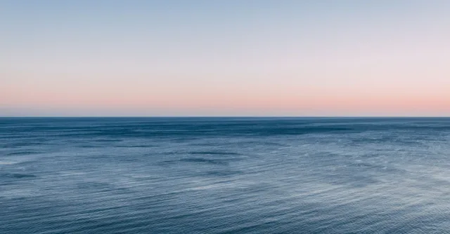 Peaceful view of the ocean at twilight with a colorful sky and calm waves.
