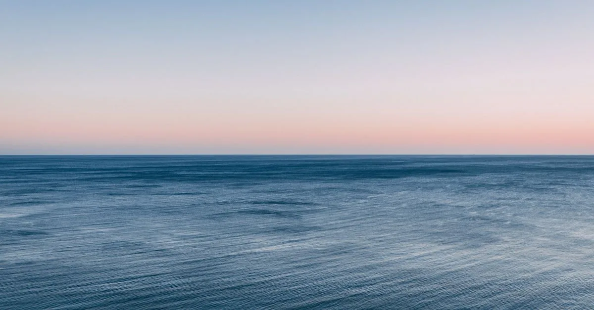 Peaceful view of the ocean at twilight with a colorful sky and calm waves.