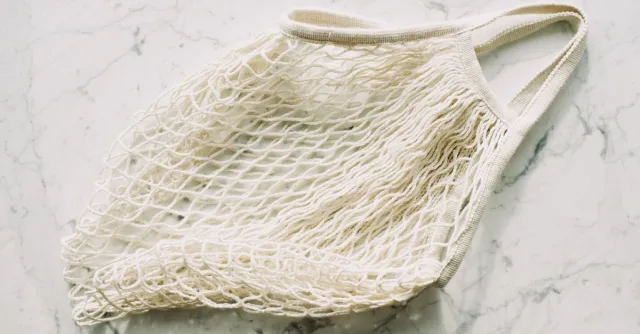Top view of simple eco friendly white mesh bag arranged on marble surface in room