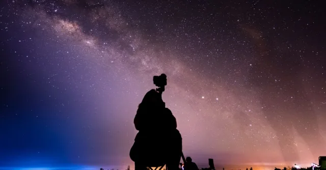 Silhouette of a stargazer with camera capturing the Milky Way under a stunning star-filled night sky.