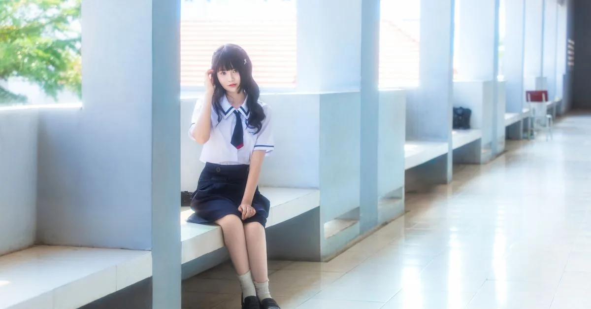Teenage girl in school uniform sitting in a bright corridor, appearing thoughtful and serene.