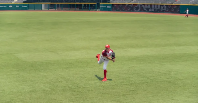 A baseball player pitching on a grass field in an empty stadium.