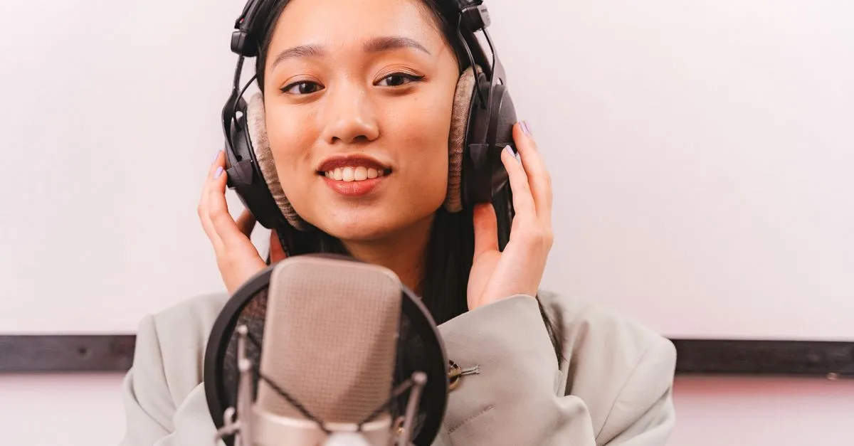 Female artist recording music in studio with condenser microphone and headphones.