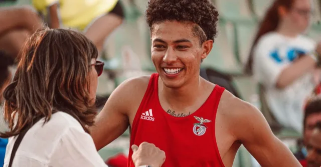Young athlete in red jersey smiling during a post-event interaction with a woman at a sports venue.