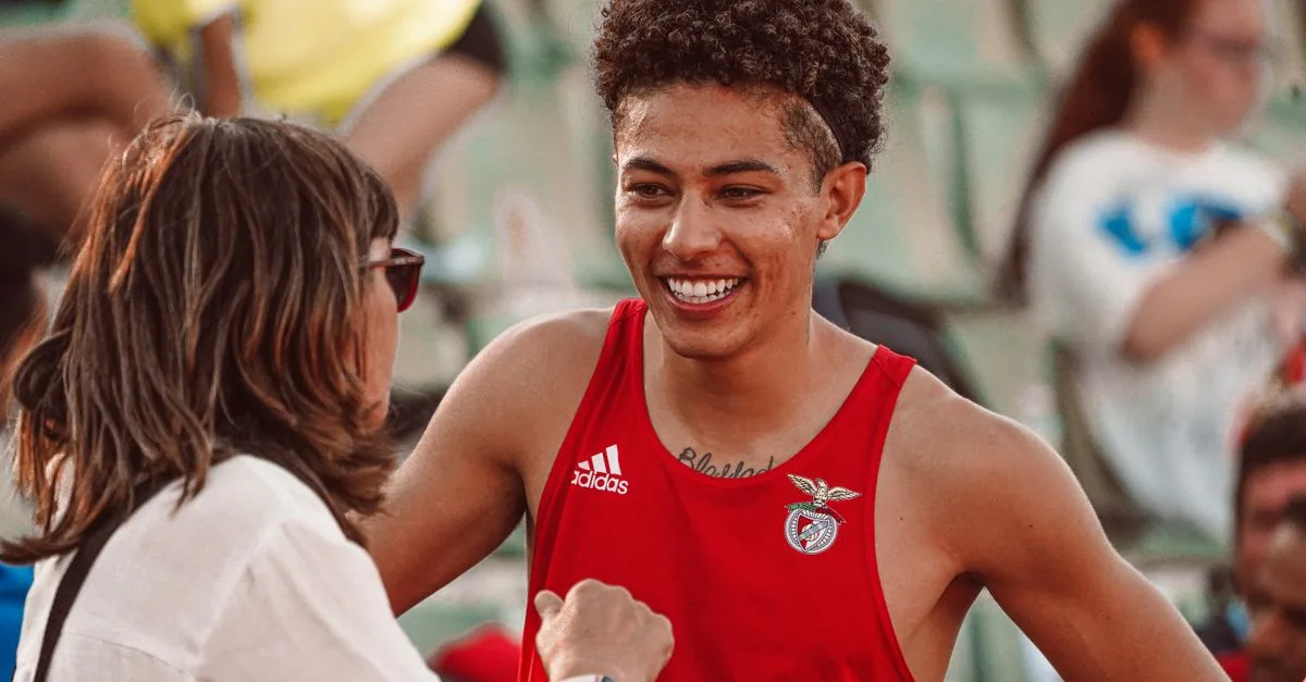 Young athlete in red jersey smiling during a post-event interaction with a woman at a sports venue.