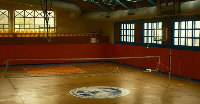 Spacious gym with volleyball net and basketball hoop, ideal for sports activities.