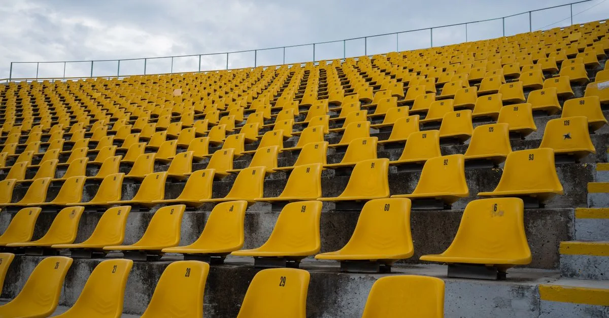 View of empty yellow seats arranged in rows at a stadium on a cloudy day.