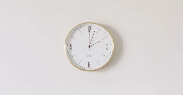 Minimalist round wall clock with gold rim and white face on a white wall.