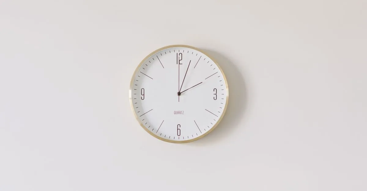 Minimalist round wall clock with gold rim and white face on a white wall.