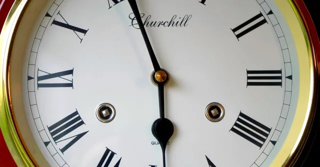 Close-up of a vintage clock face with roman numerals and gold trim, displaying classic design and elegance.
