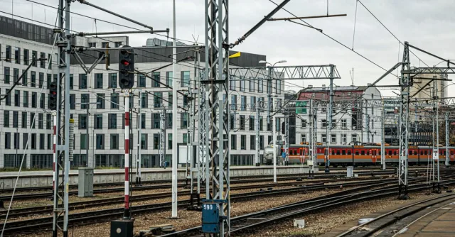 Urban train tracks and modern buildings under cloudy skies, offering a cityscape view.