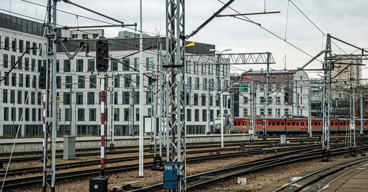 Urban train tracks and modern buildings under cloudy skies, offering a cityscape view.